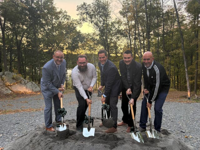 A photograph of five people holding shovels to the ground for a groundbreaking